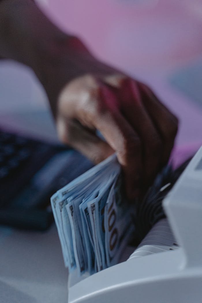 A close-up of a hand using a cash counter machine to sort bills.